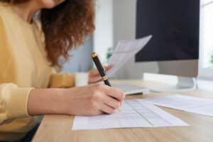 Someone holding a paper in one hand and a pen in another hand, writing on the balance sheet